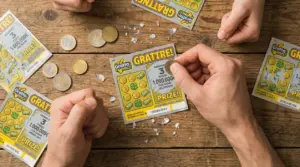 Mani che grattano biglietti Gratta e Vinci su un tavolo di legno con alcune monete.