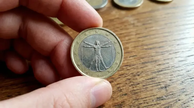 Una mano tiene una moneta da 1 euro con l'Uomo Vitruviano su sfondo di legno